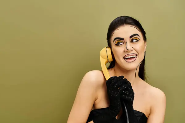 Mulher de vestido preto com telefone amarelo para orelha, apresentando maquiagem pop art e luvas pretas. — Fotografia de Stock