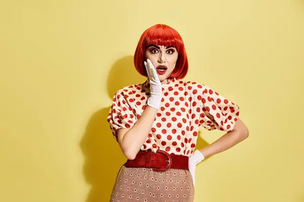 Ein lebendiger Rotschopf mit Pop-Art-Make-up und einer gepunkteten Bluse vor gelbem Hintergrund. — Stockfoto