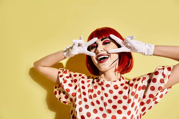 A captivating redhead woman, with pop art makeup and polka dot blouse, conceals her eyes with white gloves on a yellow background. — Stock Photo
