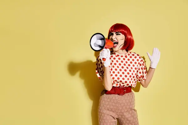 Eine grimmige rothaarige Frau mit Pop-Art-Make-up hält ein Megafon vor gelbem Hintergrund, das einer Comicfigur ähnelt.. — Stockfoto