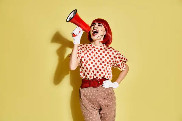 Eine selbstbewusste rothaarige Frau in Pop-Art-Make-up hält ein rot-weißes Megafon auf gelbem Hintergrund. — Stockfoto