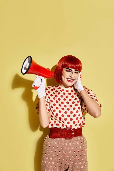 Uma mulher ruiva vibrante em blusa de bolinhas segura com confiança um megafone vermelho e branco contra um fundo amarelo. — Fotografia de Stock