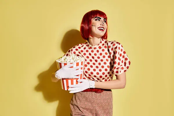 A pretty redhead woman with pop art makeup and white gloves holding a cup of popcorn, dressed in a polka dot blouse. — Stock Photo