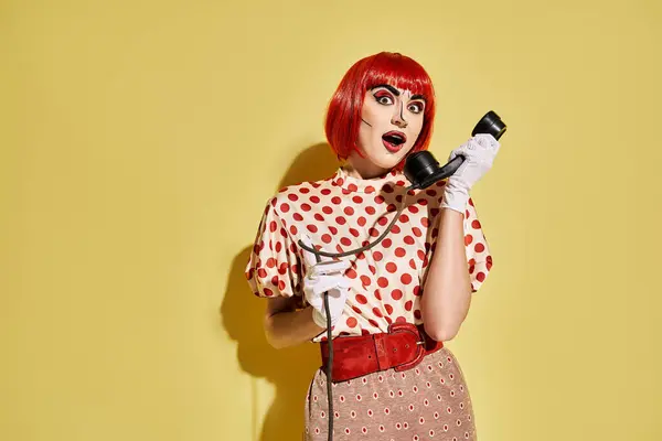 A vibrant redhead woman in pop art makeup holds a phone on a yellow background. — Stock Photo