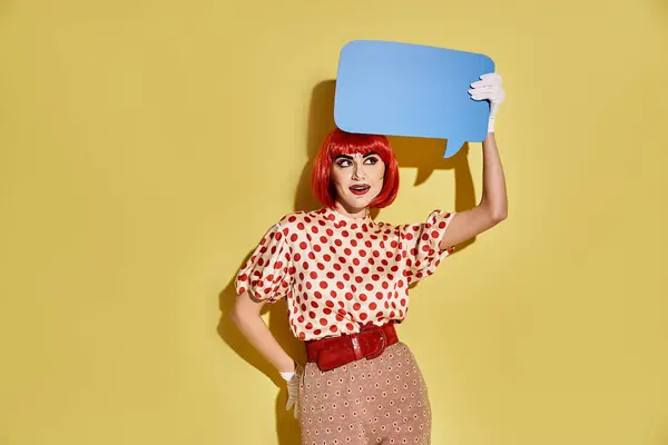 Una donna rossa creativa con trucco pop art tiene una bolla discorso blu su uno sfondo giallo. — Foto stock
