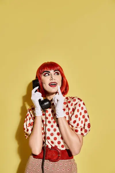 Une femme aux cheveux roux discute sur un téléphone avec maquillage pop art et chemisier à pois, sur fond jaune. — Photo de stock