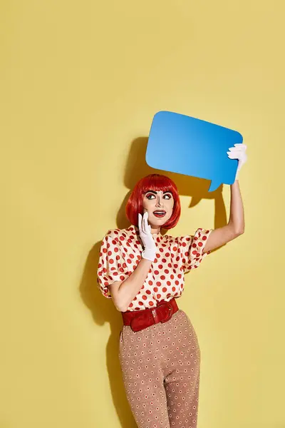 Eine hübsche rothaarige Frau mit kreativem Pop-Art-Make-up und gepunkteter Bluse hat eine Sprechblase auf dem Kopf. — Stockfoto