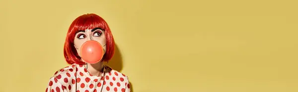 Una bella donna rossa con trucco pop art soffia una bolla, in stile come un personaggio di fumetti, su uno sfondo giallo. — Foto stock