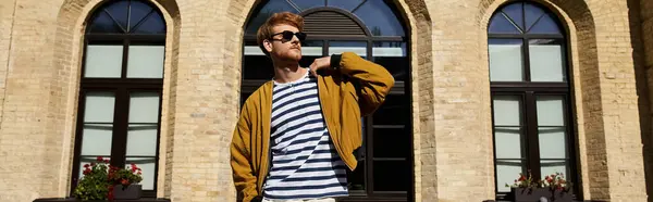 Stylish man with red hair standing confidently outside a striking building. — Stock Photo