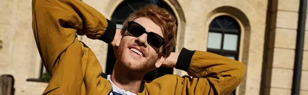 A fashionable red-haired man wearing a yellow jacket and sunglasses confidently posing for the camera. — Stock Photo