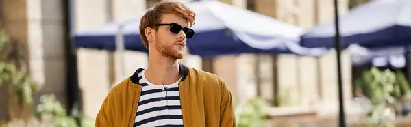 Young red-haired man in debonair attire with sunglasses walking down urban street. — Stock Photo
