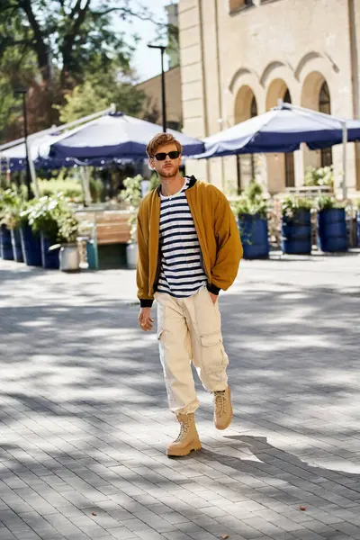 A young red-haired man in debonair attire walking down a city street next to a building. — Stock Photo