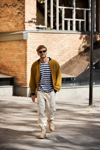 Young redhead man striding confidently in urban setting, wearing debonair yellow jacket. — Stock Photo