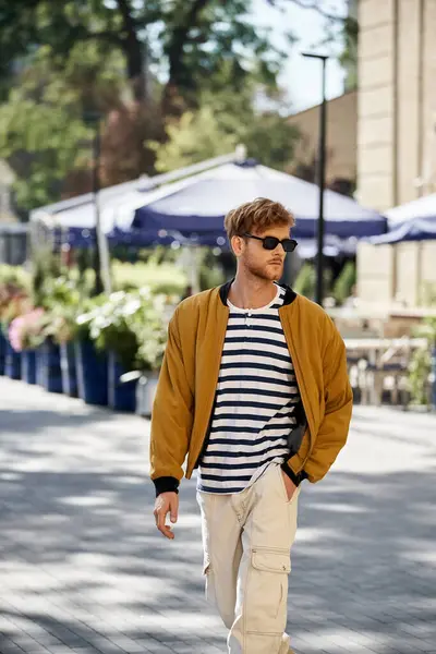 A young red-haired man walking down a city street, dressed in debonair attire and sporting sunglasses. — Stock Photo