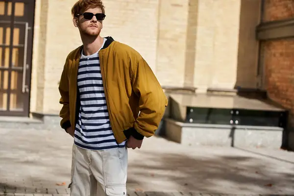Redhead man in stylish jacket and sunglasses stands on city sidewalk — Stock Photo
