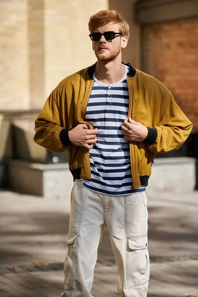A young red-haired man in trendy yellow jacket and white pants walking in the city. — Stock Photo