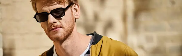 Young man with red hair strolling confidently in the city wearing sunglasses and a yellow jacket. — Stock Photo
