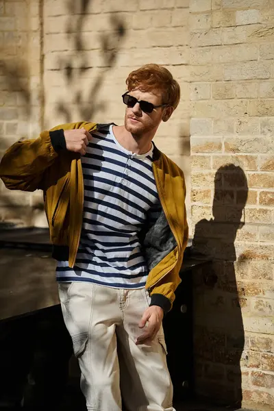 A young red-haired man in a yellow jacket and sunglasses taking a stroll in the city. — Stock Photo