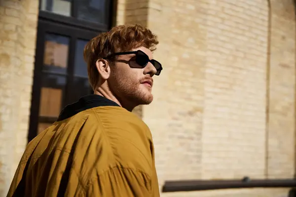 Red-haired man exudes debonair style in a yellow jacket and black sunglasses while walking in the city. — Stock Photo