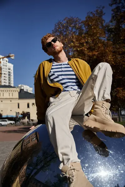 Stylish red-haired man in city, sitting atop a gleaming surface. — Stock Photo