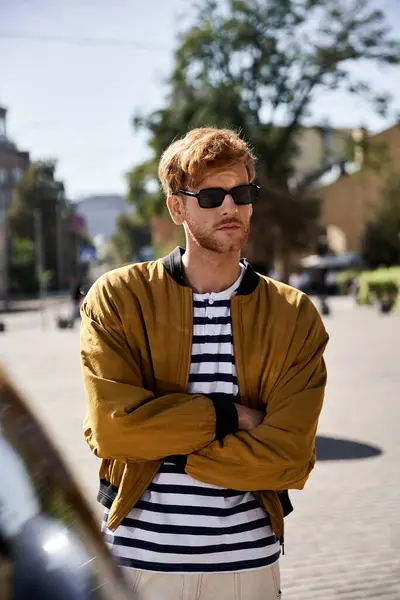 Red-haired man in debonair attire standing with arms crossed in front of an installation art. — Stock Photo