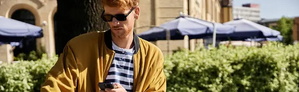 Young man in yellow jacket checks phone while strolling city streets. — Stock Photo