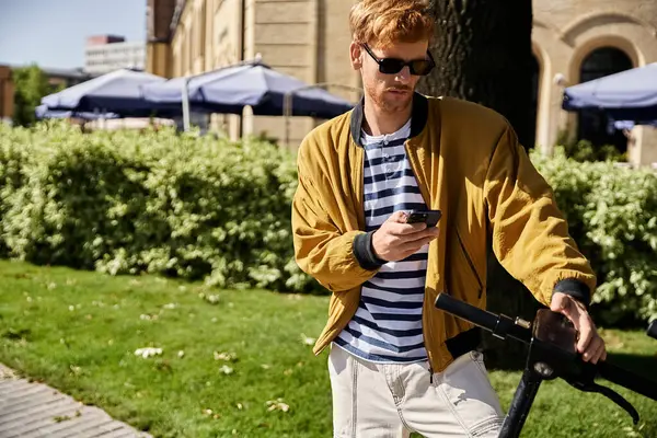 Young red-haired man in debonair attire uses cell phone while walking through the city. — Stock Photo