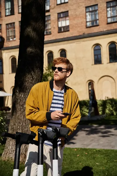 A stylish red-haired man stands near a tree in front of a building in the city. — Stock Photo