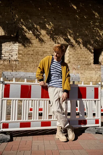 Young red-haired man in debonair attire confidently sitting on top of a white fence in the city. — Stock Photo