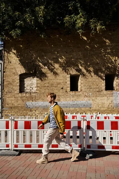 A young red-haired man in debonair attire walking down a city street next to a fence. — Stock Photo