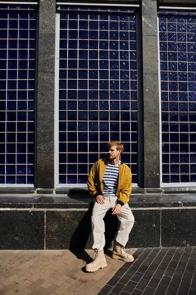 A young red-haired man in debonair attire sitting on a ledge in front of a building. — Stock Photo