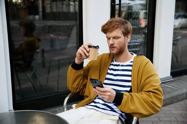 A red-haired young man in debonair attire sits in a chair, focused on his cell phone. — Stock Photo