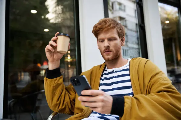 Young red-haired man in debonair attire sitting outdoors, engrossed in cellphone. — Stock Photo