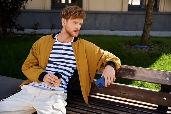 A young red-haired man in debonair attire sits on a wooden bench in a serene park setting. — Stock Photo