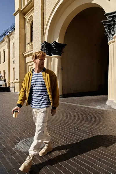 Young man with red hair walking alongside a tall building in the city. — Stock Photo