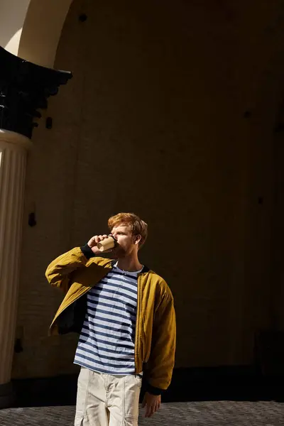 Young red-haired man in debonair attire drinking coffee outside building. — Stock Photo