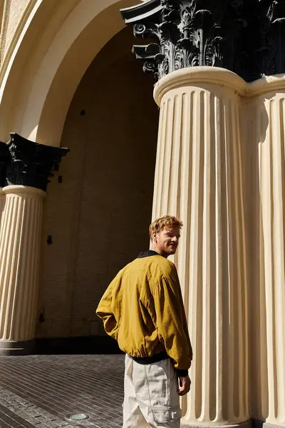 A stylish young man stands confidently in front of a majestic tall column in the city. — Stock Photo