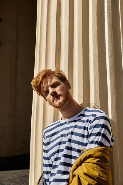 A stylish red-haired man stands beside a towering column in the city. — Stock Photo