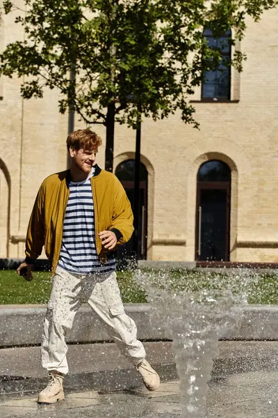 Young red-haired man in debonair attire standing in front of a water fountain. — Stock Photo
