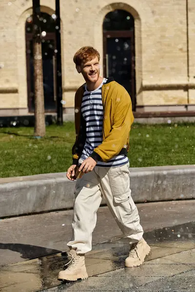 Young man with red hair walks along sidewalk in front of building. — Stock Photo