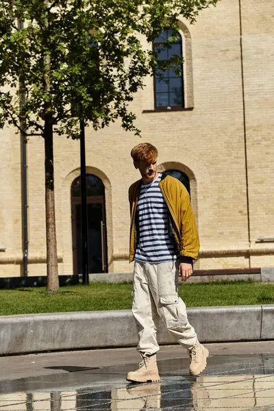 A young man with red hair walking confidently in front of a building. — Stock Photo