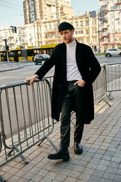 Young red-haired man leaning on fence with hands on hips in urban setting. — Stock Photo