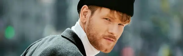 A young red-haired man with a beard, in debonair attire, strolling through the city wearing a black hat. — Stock Photo