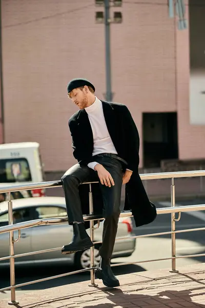 A stylish red-haired man confidently sits on a metal rail in the city. — Stock Photo