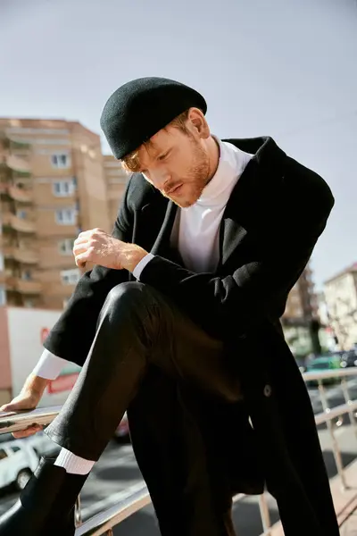 A red-haired man in debonair attire and a hat sitting gracefully on a ledge in the city. — Stock Photo
