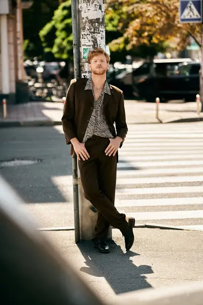 A stylish red-haired man leans against a pole on a busy city street. — Stock Photo