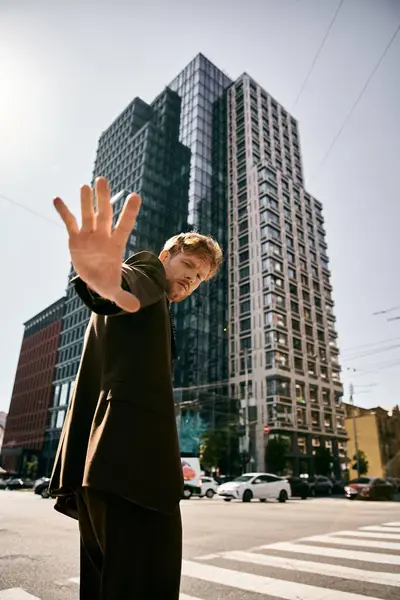 Young red-haired man standing in city street with hand raised. — Stock Photo