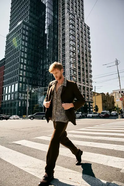 Joven hombre pelirrojo en traje de debonair caminando por la calle de la ciudad con edificios altos en el fondo. - foto de stock