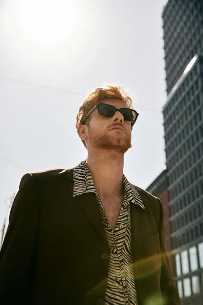 Stylish red-haired man in suit and sunglasses outside a towering building. — Stock Photo