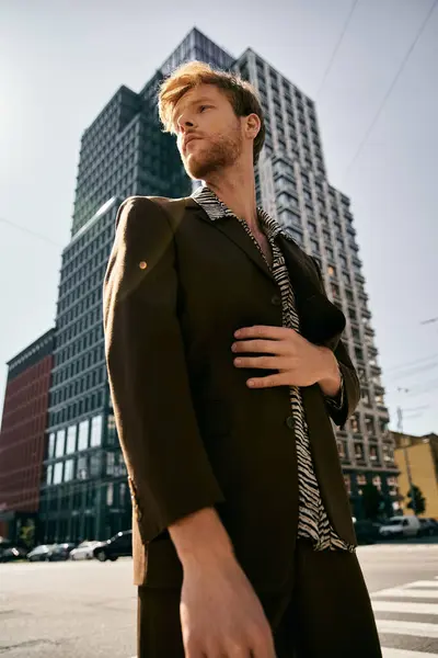 Un joven pelirrojo vestido con un atuendo desdeñoso se para con confianza frente a un imponente edificio. - foto de stock